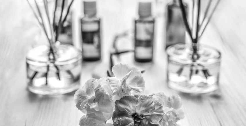 Reed diffusers and small essential oil bottles on a wooden table, with white flowers in the foreground (black-and-white photo).