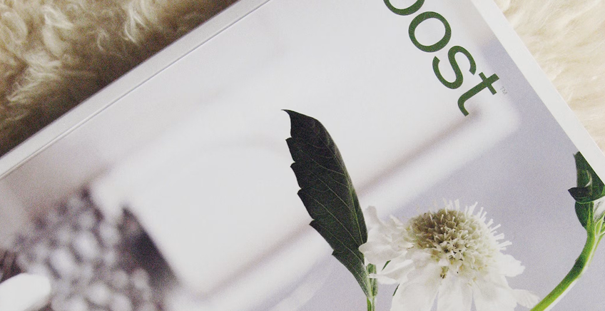 Close-up of a magazine page with a white flower and green stem on a soft background, the word 'post' partially visible at the edge.